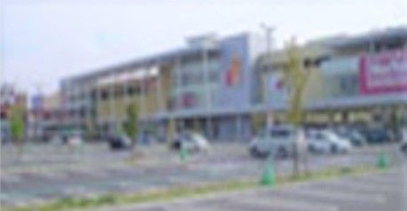 集合店舗型施設の建物の外観である。４階建てと３階建ての建物が並んでおり、前は広い駐車場になっている。