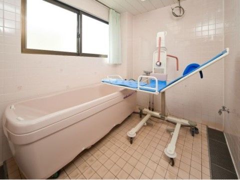 タイル張りの広い浴室に、介護浴槽が設置されている。浴槽の手前に、座ったまま入浴するための青いリフトがある。