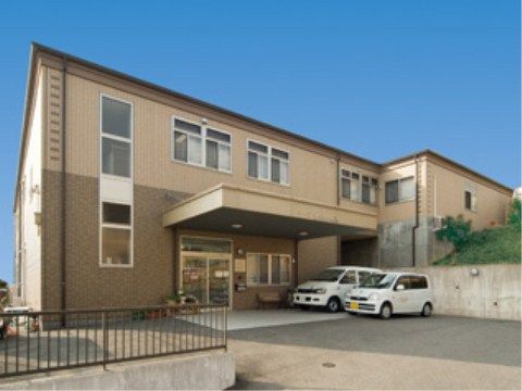 ツートンカラーの２階建ての建物。駐車場に白い車が２台停まっている。