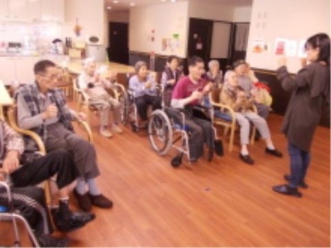 共有スペースに集まり、椅子や車椅子に座ってレクリエーションを楽しむ高齢者の様子。