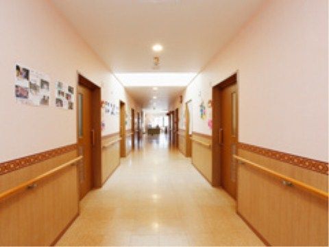 真っ直ぐな廊下は、両側に居室ドアが並んでいる。壁には手すりが付いており、白い壁には写真付きの掲示物がある。