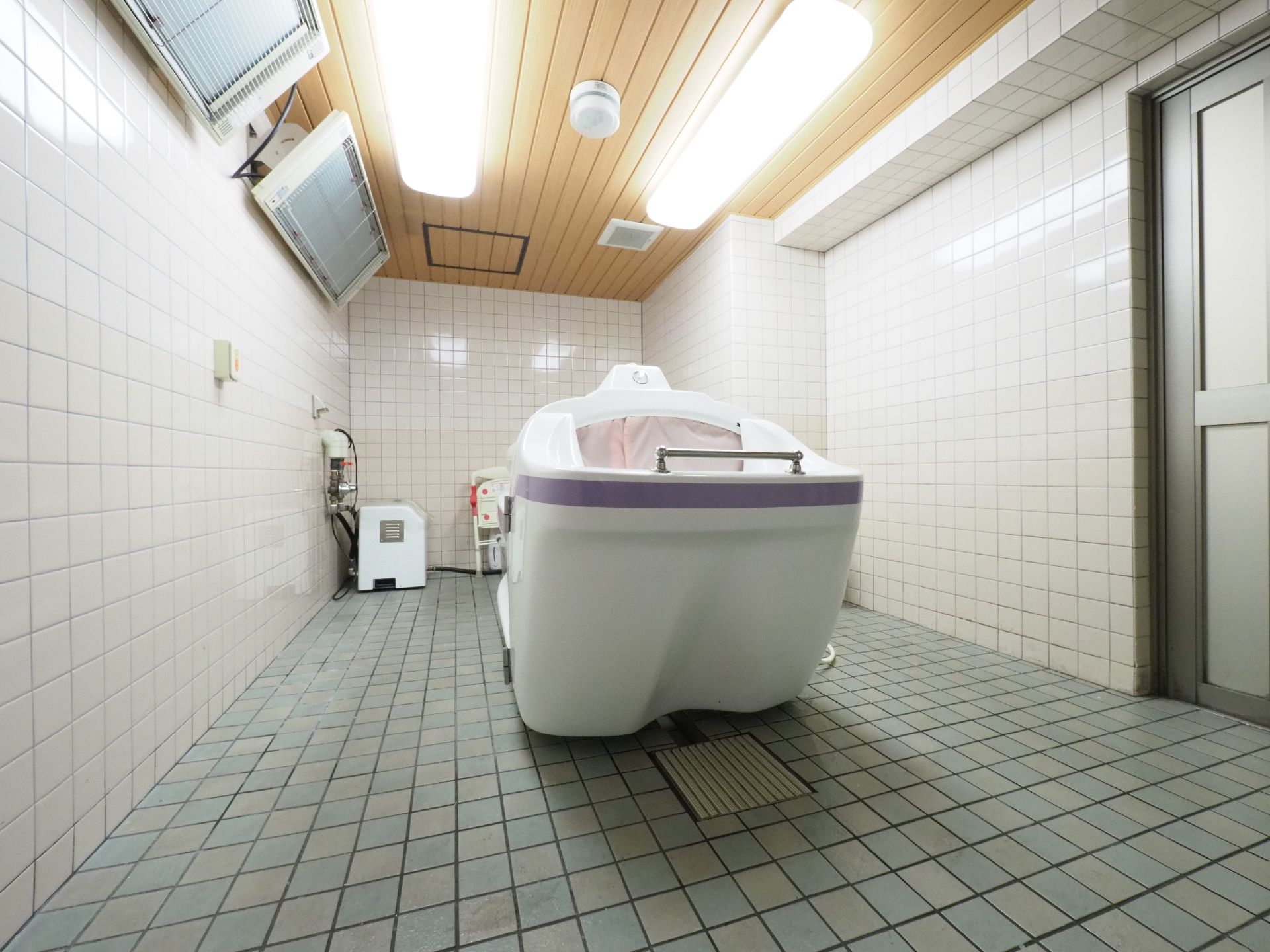 壁と床はタイルを使用していて奥には介助用の椅子や機械が置かれている。天井付近にはヒーターが設置されている。