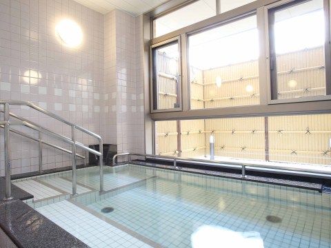 数人が湯船に浸かれる広さの浴槽は、水色のタイル調である。横一面ガラス張りで、日本庭園を眺めながら入浴をお楽しみいただける大浴場である。