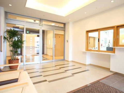ガラス張りの自動ドアを採用した広々としたエントランスである。横側にスタッフルームの木枠の窓口を設けている。